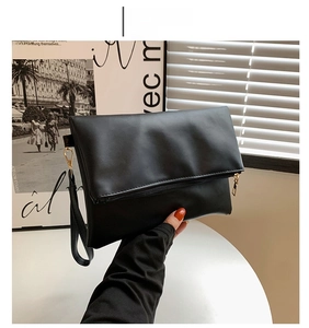 Detalle del bolso de sobre negro mate con cremallera metálica y correa ajustable