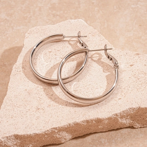 Detailed view of polished silver hoop earrings resting on a textured minimalist stone base