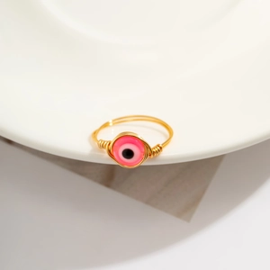Macro shot of gold wire-wrapped ring featuring a pink evil eye charm on a white background