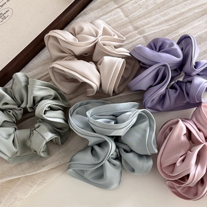 Five large satin scrunchies in Morandi colors like beige and lavender on linen background