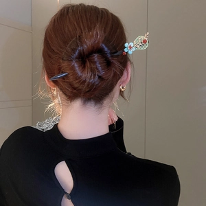 Detail of a floral hair stick with blue flowers and golden leaves in a classic hairstyle