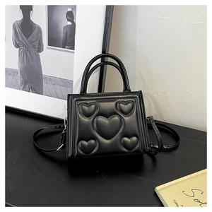 Détail du sac à main carré noir avec motifs de cœurs matelassés en relief et poignée