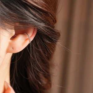 Macro shot of silver ear cuff with textured woven pattern on female model's ear