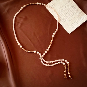 Detail of vintage long pearl necklace with silver clasp and double tassel on brown silk fabric