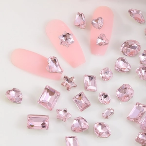 Close-up of pink crystal nail art charms in heart and star shapes on pink manicured nails