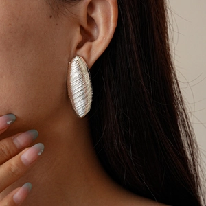 Close-up of brushed silver oval stud earring with spiral texture on female model
