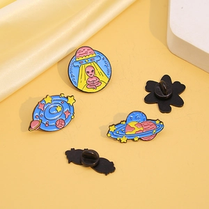 Three enamel space pins featuring an alien in a UFO and planets on yellow fabric