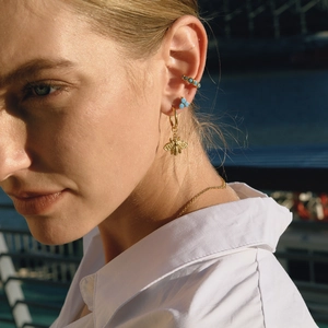 Close-up of gold bee pendant earring and turquoise ear cuffs worn by a model