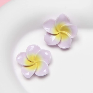 Macro detail of light purple resin frangipani flower earrings in a white ceramic dish