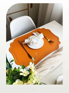 Detail of scalloped orange faux leather placemat with refined lychee grain texture