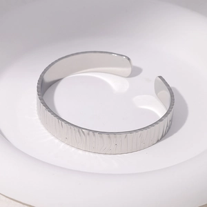 Adjustable silver stainless steel open bangle with unique wood grain texture on a tray