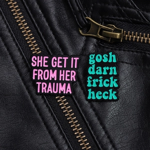 Detail of enamel lapel pins with text on black leather jacket with metal zippers