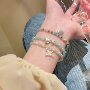 Nahaufnahme der Perlenarmbänder mit Delfin-, Seestern- und Muschelanhängern am Handgelenk