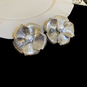 Macro detail of large silver flower earrings with white pearl and brushed metal texture