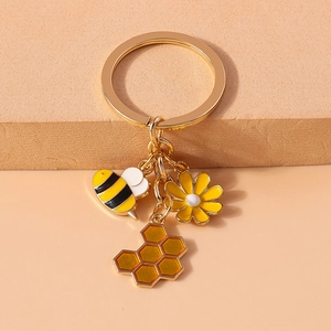 Close-up of golden bee keychain featuring enamel daisy, bee and honeycomb charms