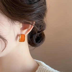 Close-up of elegant square orange enamel earrings with gold trim worn by a model
