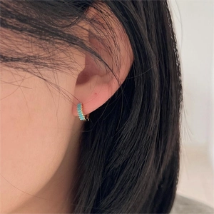 Close-up of gold huggie earrings featuring a row of rectangular turquoise stones