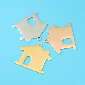 Three mirror-polished house pendants in silver, gold, and rose gold on blue background