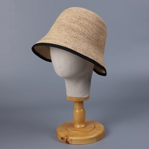 Minimalist raffia straw bucket hat in khaki with black trim on a display head stand