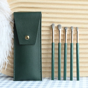 Detailed view of 5-piece green makeup brush set with leather pouch on a textured background