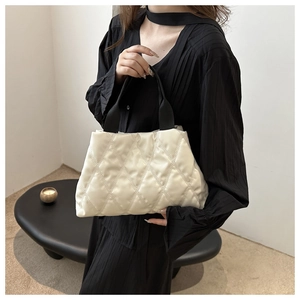 Close-up of quilted white puffer tote bag with black strap held by a fashion model