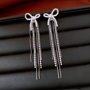 Macro detail of silver bow tassel earrings with sparkling crystals on leather stand