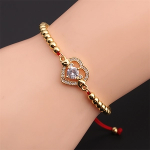 Detail of golden heart bracelet with white zircon and adjustable red cord on wrist