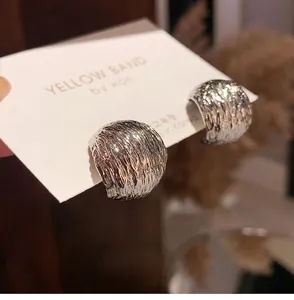 Close-up of silver earrings with irregular lava texture and metallic glossy finish