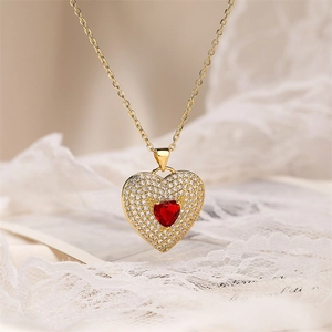 Macro shot of gold heart necklace with red gem and clear zircon pavé on white lace
