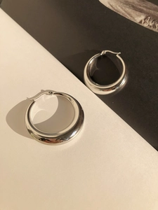 Macro detail of thick silver hoop earrings featuring a polished streamlined hollow design
