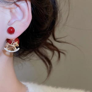 Detail of red gold-plated horse pendant earring with cubic zirconia on model ear