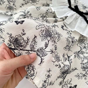 Detail of floral baby top featuring white ruffle collar and black velvet bow accent