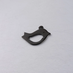 Close-up of a polished black bird-shaped pendant with a hanging ring on a textured surface