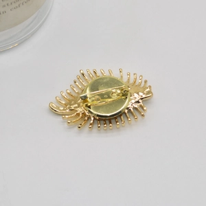 Golden metal evil eye brooch with radial eyelashes and pin closure on white background