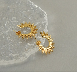 Macro detail of gold sunray C-shape stud earrings on a textured glass display tray