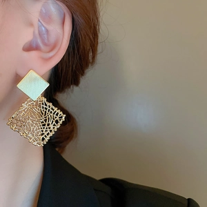 Close-up of golden geometric square earrings with mesh texture and brushed finish on model