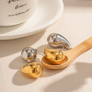 Polished gold and silver teardrop earrings displayed on a wooden spoon with textile background