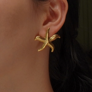 Golden starfish stud earring with realistic texture worn by a model in a summer style