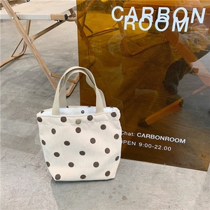 Detail of a beige corduroy mini tote bag with brown polka dots and a metal snap closure