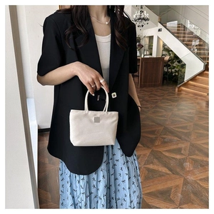 Sac seau en nylon beige porté par un mannequin en blazer noir à manches courtes