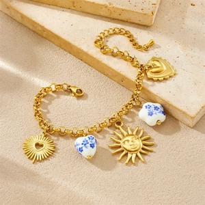 Gold plated heart and sun charm bracelet with vintage floral ceramic pendants on stone