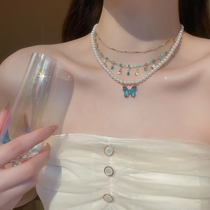 Detailed view of layered necklace set with blue butterfly pendant and pearls on model