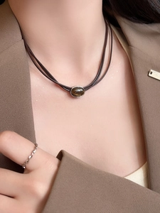 Close-up of brown tiger eye stone pendant necklace on a model wearing an autumn blazer