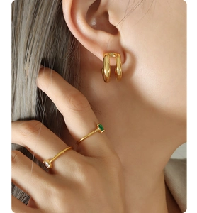 Close-up of elegant gold double-hoop earrings and rings with green and white gems
