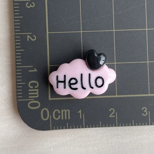 Détail d'une breloque nuage rose en résine avec texte Hello noir et petit cœur noir