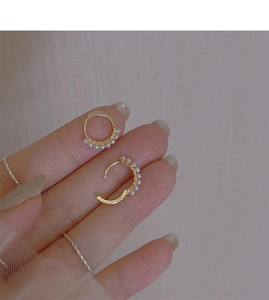 Detailed close-up of a gold pearl hoop earring held by hand to show its small size