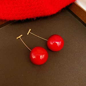 Detail view of red cherry earrings with gold metal stems on dark background