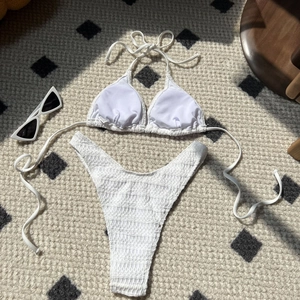 Flat lay of white smocked fabric bikini set with sunglasses on a textured rug