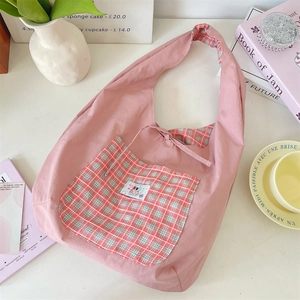 Detail view of pink hobo shoulder bag featuring a plaid pocket and reversible design