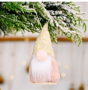 Detail eines rosa Weihnachts-Wichtels mit goldener Strickmütze an verschneiten Zweigen